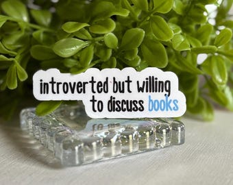 May include: White sticker with the text "introverted but willing to discuss books" in black and blue lettering. The sticker is on a clear glass surface.