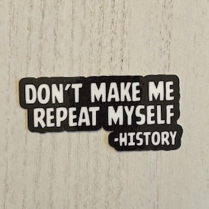 May include: A black and white sticker with the text "DON'T MAKE ME REPEAT MYSELF -HISTORY". The sticker has a rectangular shape with rounded corners and is placed on a light-colored wooden surface.