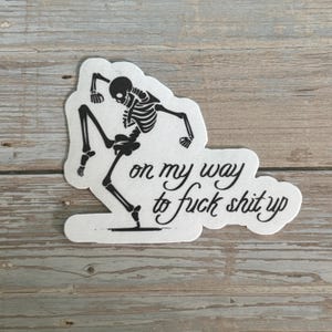 K&ouml;nnte beinhalten: Ein gestanzter Aufkleber mit einer schwarzen Skelett-Illustration in einer dynamischen Pose. Der wei&szlig;e Hintergrund zeigt den Schriftzug "on my way to fuck shit up" in einer kursiven Schrift.