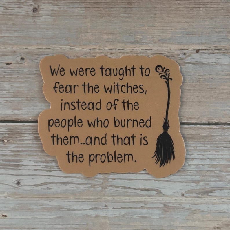 May include: A tan-colored sticker with black text that reads, "We were taught to fear the witches, instead of the people who burned them...and that is the problem." A black witch's broom is on the right.