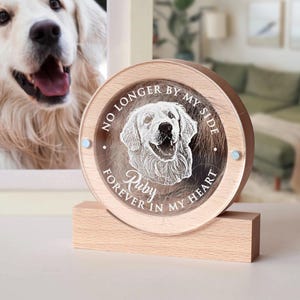 May include: A framed photograph of a Golden Retriever next to a wooden memorial. The memorial is a round, clear acrylic piece with a laser-etched image of a dog and the words "NO LONGER BY MY SIDE FOREVER IN MY HEART" and the name "Ruby".