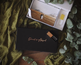 May include: A black box with the names "Daniel & Abigail" in gold lettering, a white box with a photo of a couple in a field, and a yellow USB drive.