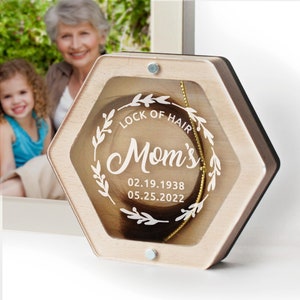 May include: A wooden hexagonal box with a clear lid, displaying a lock of hair inside. The box is engraved with the text "Lock of Hair Mom's 02.19.1938 05.25.2022".