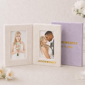 May include: A double-sided cream velvet photo frame featuring gold text that reads JASON HEART EMILY, displayed next to a closed lavender velvet photo album with gold text reading JASON HEART EMILY and MAY 15, 2026 on the front cover.