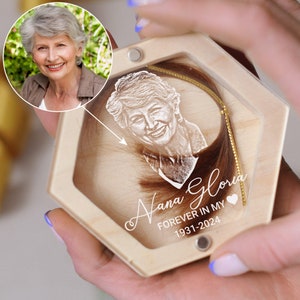 May include: A wooden box with a clear lid containing a lock of hair and a photo of a woman. The box is engraved with the text "Nana Gloria Forever in My Heart 1931-2024".