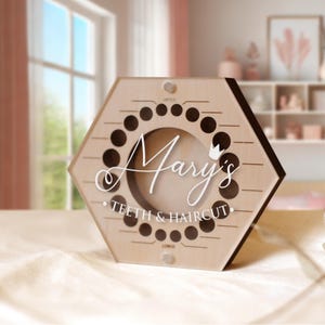 May include: A hexagonal wooden keepsake box featuring a circular centre cutout and a series of small holes arranged in a ring. The front is printed with the text "Mary's TEETH & HAIRCUT" in white script and block lettering, along with a small crown icon.