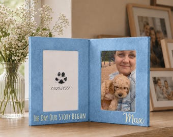 May include: A light blue, bi-fold photo frame with two openings. One side features a paw print and the date 03.25.2022, with the text "THE DAY OUR STORY BEGAN". The other side holds a photo with the name "Max".