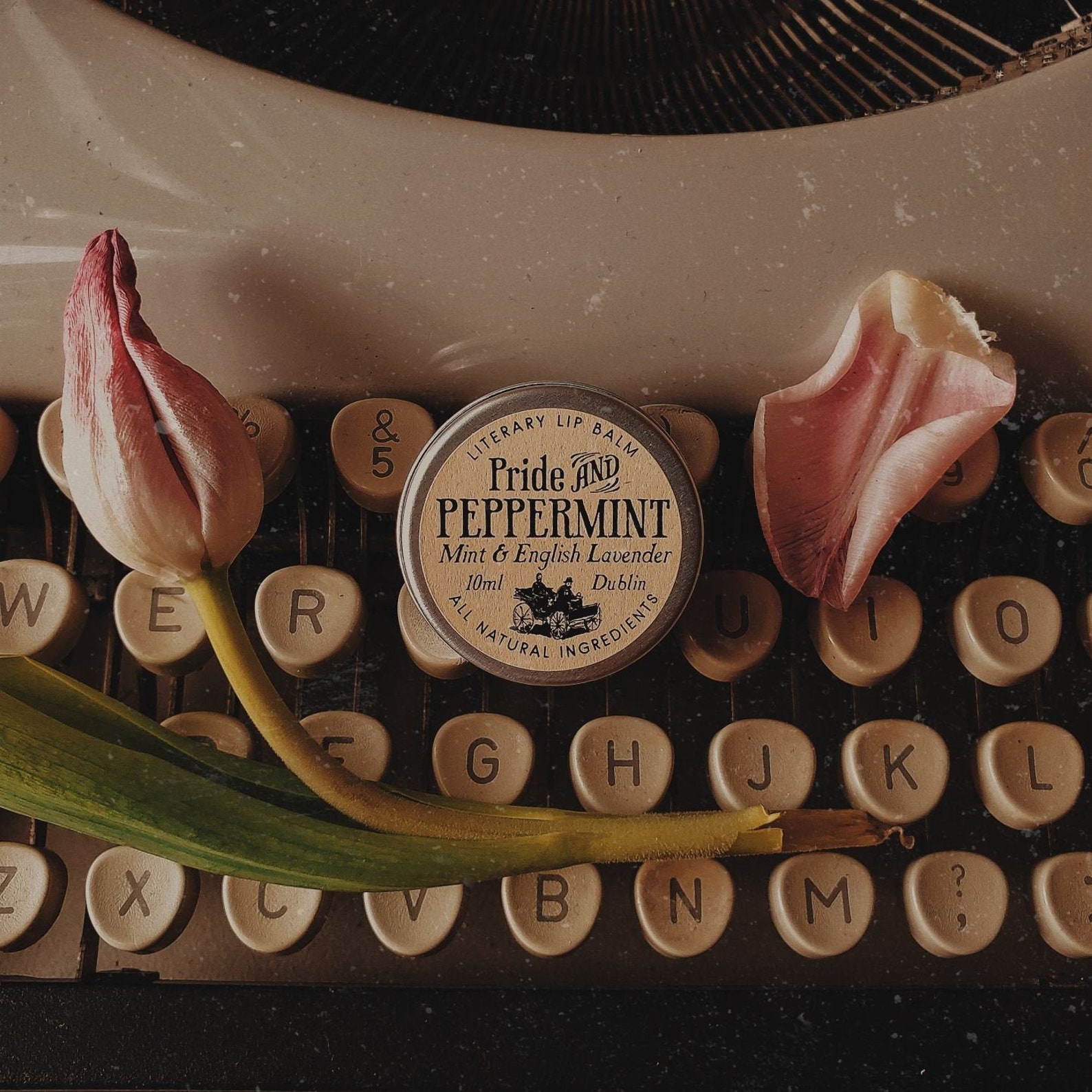 Pride and peppermint lip balm on top of older style typewriter with flower petals 