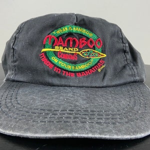 Puede incluir: Gorra de béisbol negra con un logotipo bordado en verde, amarillo y rojo que dice "Mambo Brand Goods" y "Made in the Bahamas".