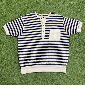 Peut inclure: Un t-shirt à manches courtes rayé avec un col boutonné et une poche plaquée sur le côté gauche. Le t-shirt est blanc et bleu marine.