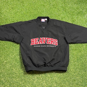 May include: Black Oregon State Beavers pullover jacket with a V-neck and long sleeves. The word "BEAVERS" is in red block letters with a white outline, above "OREGON STATE UNIVERSITY" in red.
