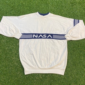 May include: White long-sleeve shirt with blue and white striped trim and the word "NASA" in blue lettering.