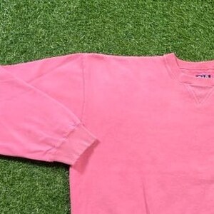 May include: A pink long-sleeved sweatshirt with a crew neck. The sweatshirt has a small blue tag on the back of the neck that says "Gildan".