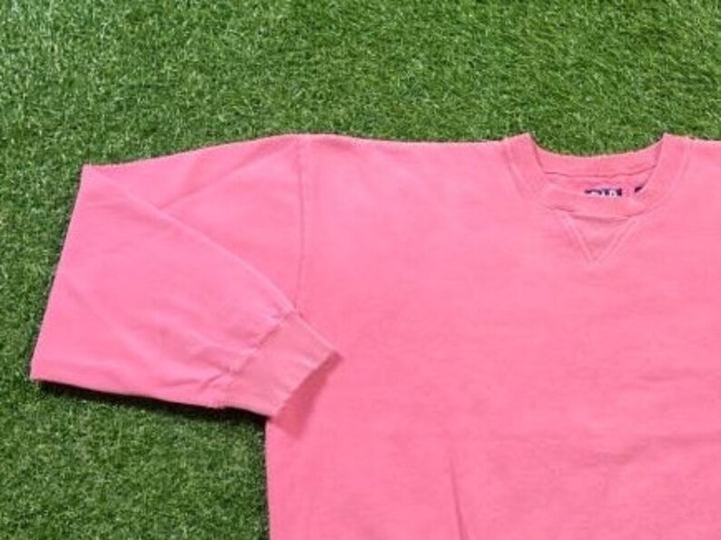 May include: A pink long-sleeved sweatshirt with a crew neck. The sweatshirt has a small blue tag on the back of the neck that says "Gildan".