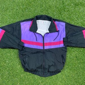 May include: A black windbreaker jacket with purple and pink color blocking. The jacket has a zipper closure and a drawstring hood.