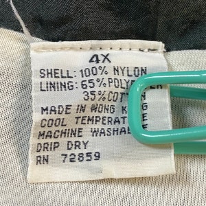 Może przedstawiać: Biała metka z czarnym tekstem, kt&oacute;ry brzmi: "4X", "SHELL: 100% NYLON", "LINING: 65% POLY", "35%COT", "MADE IN HONG K", "COOL TEMPERAT", "MACHINE WASHAL", "DRIP DRY", "RN 72859".