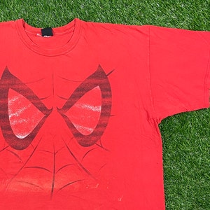 Puede incluir: Camiseta roja con un estampado gr&aacute;fico en blanco y negro de la m&aacute;scara de Spider-Man.