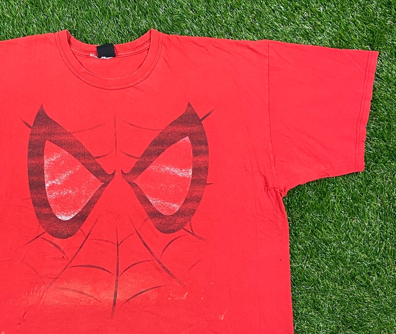 Puede incluir: Camiseta roja con un estampado gr&aacute;fico en blanco y negro de la m&aacute;scara de Spider-Man.