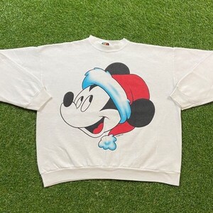 Könnte beinhalten: Weißer Weihnachtspullover mit einem Cartoon-Bild von Mickey Mouse, der einen Weihnachtsmann-Hut trägt. Der Pullover hat einen Rundhalsausschnitt und lange Ärmel.