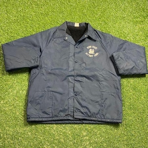 Puede incluir: Chaqueta azul marino de los Penn State Nittany Lions. La chaqueta tiene cierre de botones, cuello y dos bolsillos delanteros. El logotipo de Penn State está bordado en el pecho izquierdo. La chaqueta está sobre una superficie verde.