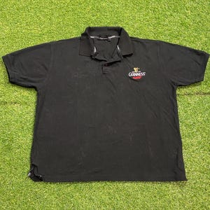May include: Black polo shirt with a collared neckline and short sleeves. The Guinness logo is embroidered on the chest. The shirt is made of a soft material, suitable for casual wear. A classic design.