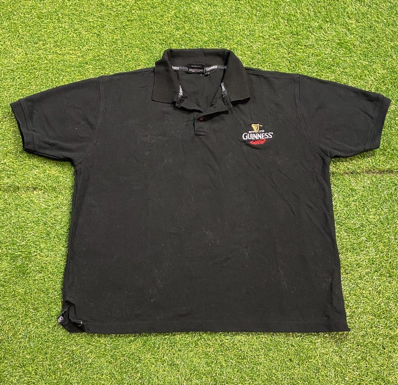 May include: Black polo shirt with a collared neckline and short sleeves. The Guinness logo is embroidered on the chest. The shirt is made of a soft material, suitable for casual wear. A classic design.