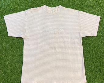 Könnte beinhalten: Ein rosa-weiß gestreiftes T-Shirt mit dem gestickten Schriftzug "GUESS JEANS" auf der Vorderseite.