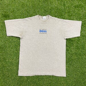 Op de afbeelding: Een grijs T-shirt met een blauw Dell-logo en de tekst "Be Direct" en "www.dell.com".
