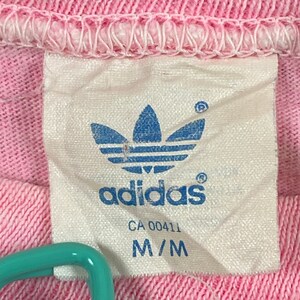 Peut inclure: Une &eacute;tiquette blanche avec un logo Adidas bleu et le texte "adidas" en bleu. L'&eacute;tiquette comprend &eacute;galement le texte "CA 00411" et "M/M".