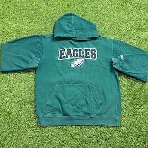 Könnte beinhalten: Grüner Kapuzenpullover mit dem Wort "EAGLES" in weißer und schwarzer Schrift auf der Brust. Unter dem Wort "EAGLES" befindet sich ein weißes und graues Adlerlogo. Der Pullover hat eine Vordertasche und eine Kapuze.