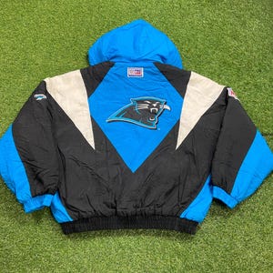 Peut inclure: Veste vintage des Panthers de la Caroline, noire, bleue et blanche. La veste pr&eacute;sente le logo de l'&eacute;quipe au dos, une capuche bleue et un design noir et blanc. La veste a un ourlet et des poignets c&ocirc;tel&eacute;s.