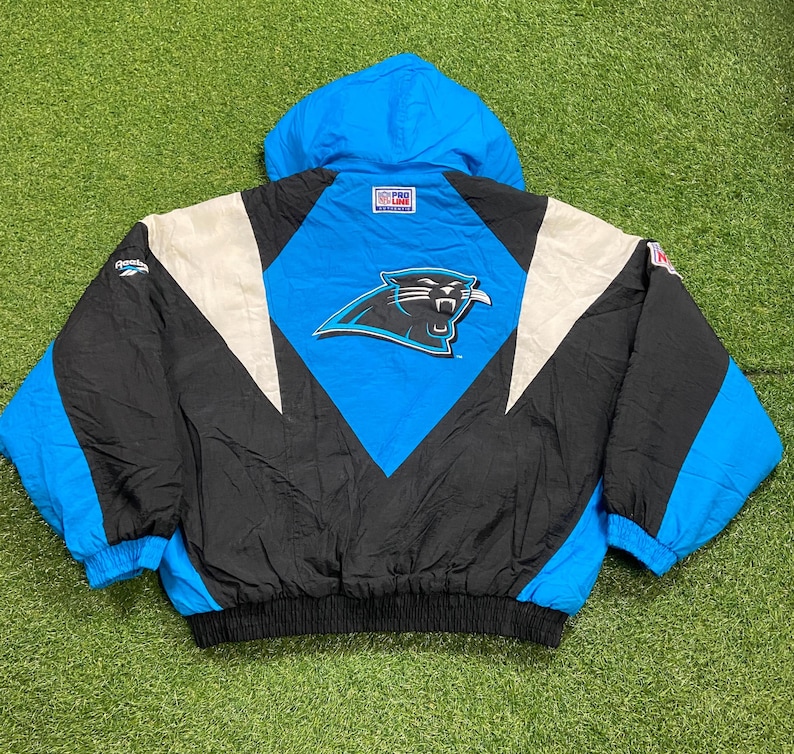Peut inclure: Veste vintage des Panthers de la Caroline, noire, bleue et blanche. La veste pr&eacute;sente le logo de l'&eacute;quipe au dos, une capuche bleue et un design noir et blanc. La veste a un ourlet et des poignets c&ocirc;tel&eacute;s.