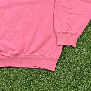 May include: Pink sweatshirt with long sleeves and a ribbed hem. The sweatshirt is made of a soft, comfortable fabric.