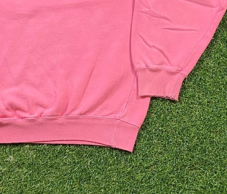 May include: Pink sweatshirt with long sleeves and a ribbed hem. The sweatshirt is made of a soft, comfortable fabric.