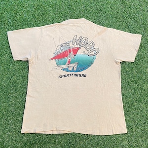 May include: A beige t-shirt with a graphic of a red boat with the text "HOBO SPORTFISHING" on the back.