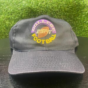 May include: A black baseball cap with a curved brim. The cap features a circular logo with the text "COLLEGE FOOTBALL" in yellow and "ESPN" in white and brown.
