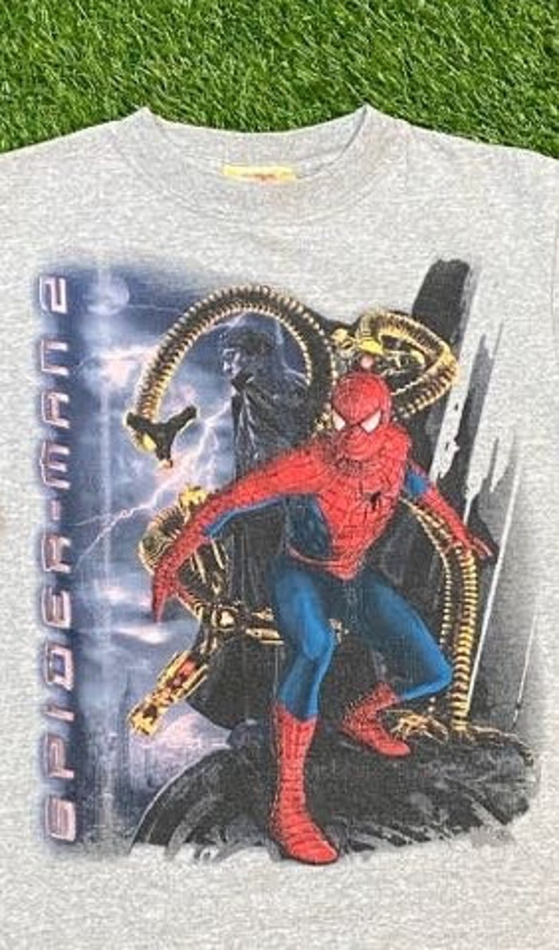 May include: Grey t-shirt featuring a graphic print of Spider-Man and Doc Ock from the film Spider-Man 2. The text "Spider-Man 2" is printed on the left side of the shirt.