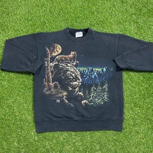 May include: Black sweatshirt with a graphic print of a wolf howling at the moon in a forest setting. The graphic is in shades of brown, green, blue, and yellow.