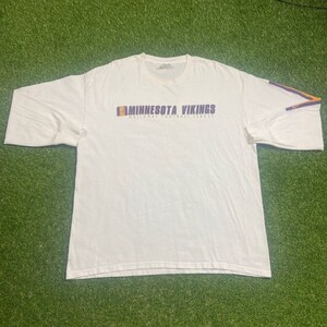 May include: White long-sleeve t-shirt with a purple and gold Minnesota Vikings logo and the text "National Football League".