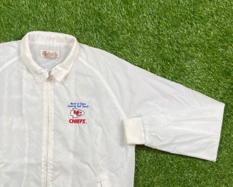May include: White windbreaker jacket with a red, white, and blue Kansas City Chiefs logo and the text "North of Dixie County Golf Classic" and "CHIEFS".
