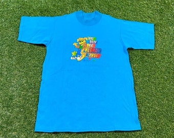 May include: A light blue t-shirt with a crew neck and short sleeves. The shirt features a colorful graphic with the text "Yo Soy El Hermano Mayor" and cartoon characters. The shirt is made of a soft material.