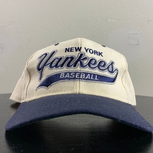 May include: A white baseball cap with a navy blue brim. The front of the cap features the text "New York Yankees Baseball" in navy blue embroidery.
