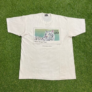May include: White t-shirt with a graphic of a white Bengal tiger on a postage stamp. The stamp says "USA 29" and "White Bengal Tiger" and "Endangered Species".