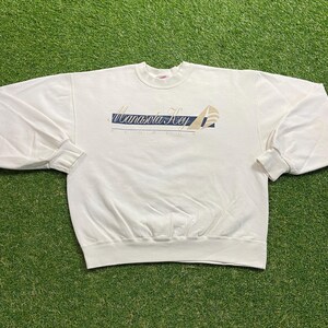 Puede incluir: Sudadera de color crema con mangas largas y puños acanalados. La parte delantera presenta el texto "Manasota Key Florida" en un diseño azul marino y beige. La sudadera está hecha de un material suave y tiene cuello redondo.