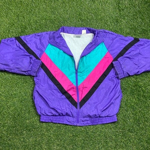 May include: A purple windbreaker jacket with a black, pink, and turquoise chevron pattern. The jacket has a zipper closure and a ribbed hem.
