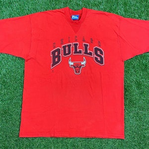 May include: Red short-sleeved t-shirt with the Chicago Bulls logo in black and white. The logo features a red bull with black horns and a white outline.
