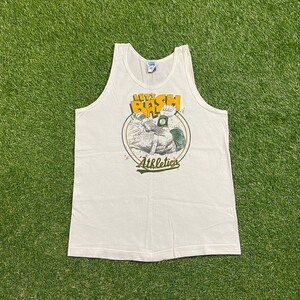 May include: White tank top with a graphic featuring the text "LET'S BASH" in yellow and green, along with the word "Athletics" in green. The graphic includes a cartoon image of a muscular arm. The tank top is made of a soft material.