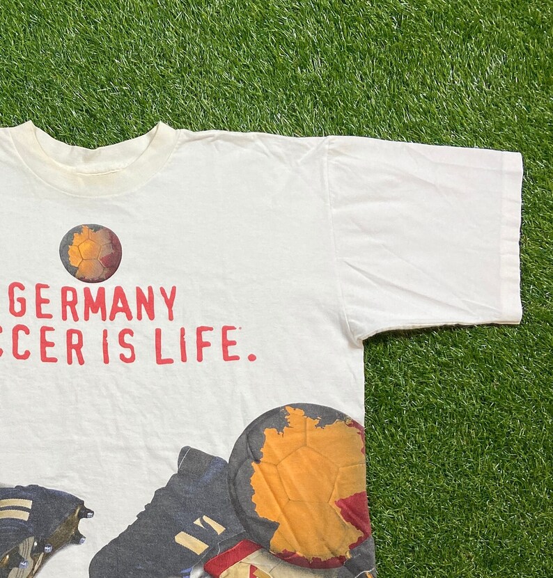 May include: White t-shirt with a red and black graphic print of a soccer ball with the text "GERMANY SOCCER IS LIFE."