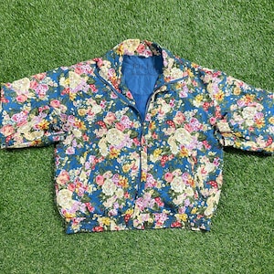 May include: A blue floral print jacket with a zipper closure. The jacket has a stand-up collar and long sleeves. The fabric is lightweight and has a silky feel.