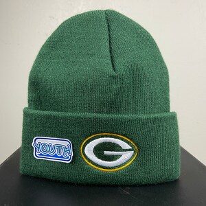 Puede incluir: Gorro de punto verde con una "G" blanca bordada en un círculo verde y dorado. El gorro también tiene un parche azul y blanco que dice "YOUTH".